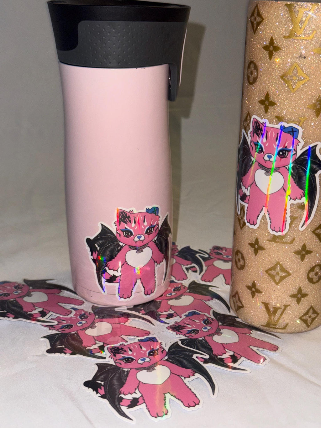 Holographic Tommi the Batcat sticker on gold glitter tumbler showing reflective rainbow shine on various tumblers