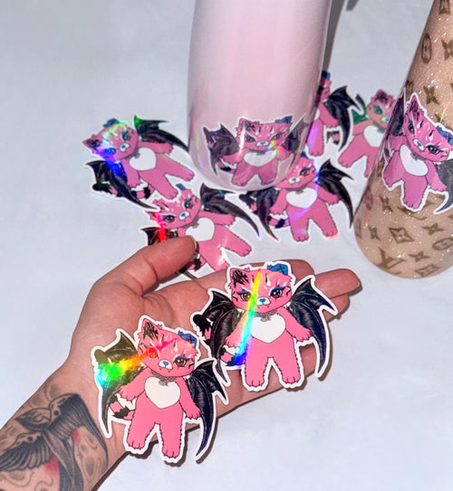 Hand holding two holographic Tommi the Batcat stickers showing rainbow color shifting effect